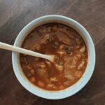 A white bowl with original cabbage soup in it and a wooden spoon