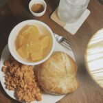 Tomato scrambled eggs with croissant and a side of fruit on a white plate