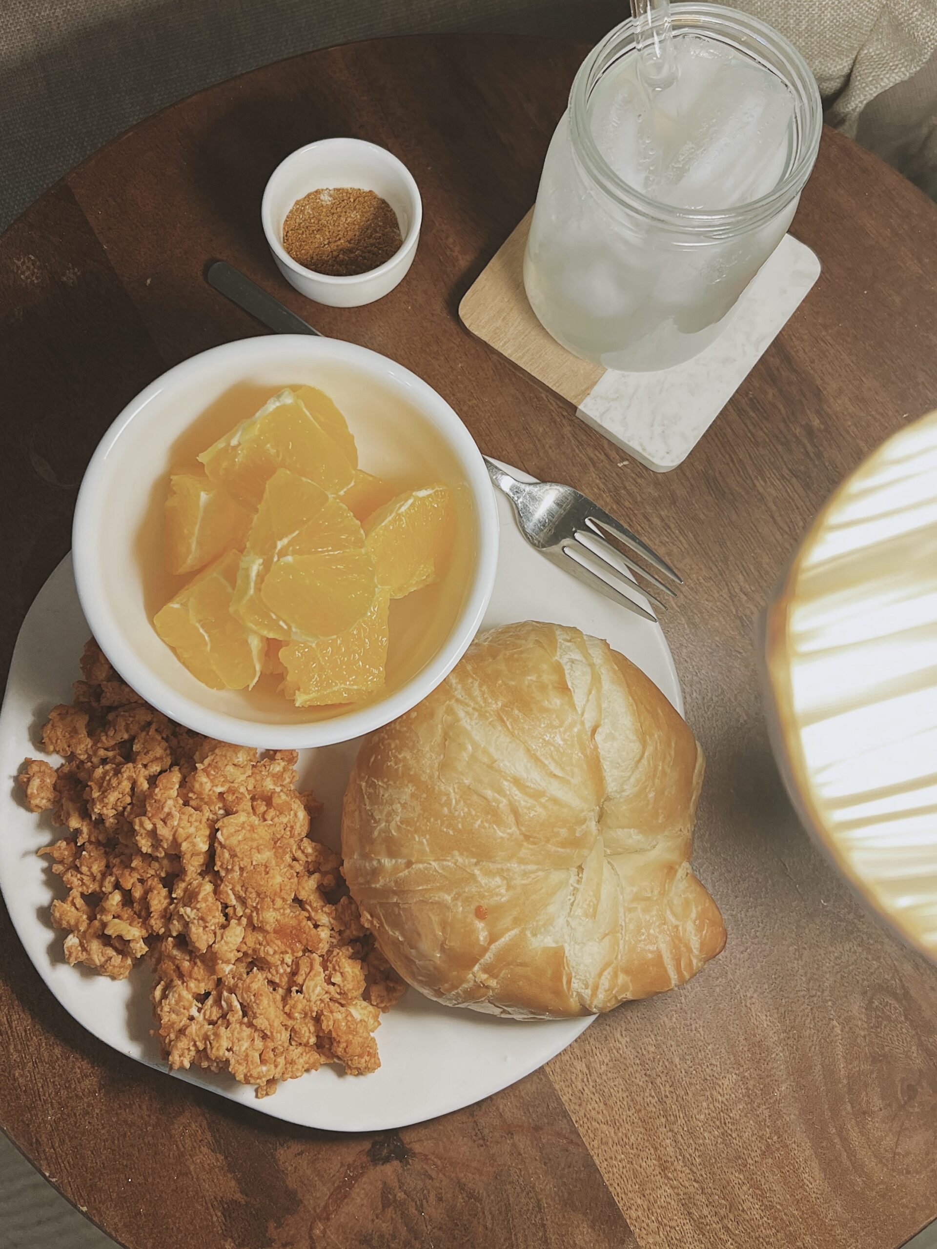 Tomato scrambled eggs with croissant and a side of fruit on a white plate