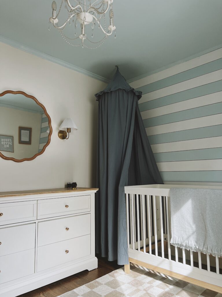 Boy's nursery with blue canopy, round mirror, sconces, white crib and dresser